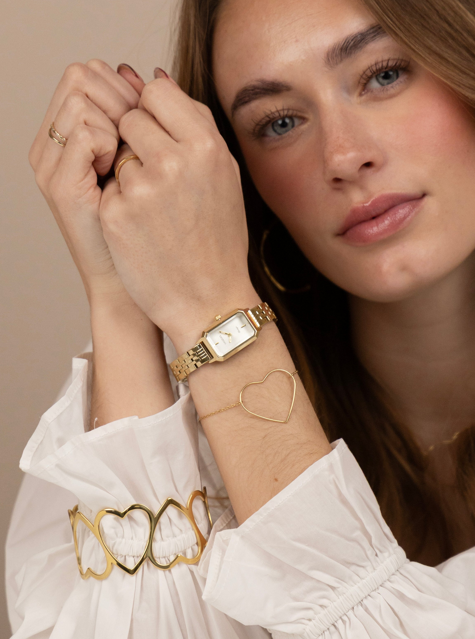 Woman wearing a gold watch and bracelet with a neutral background